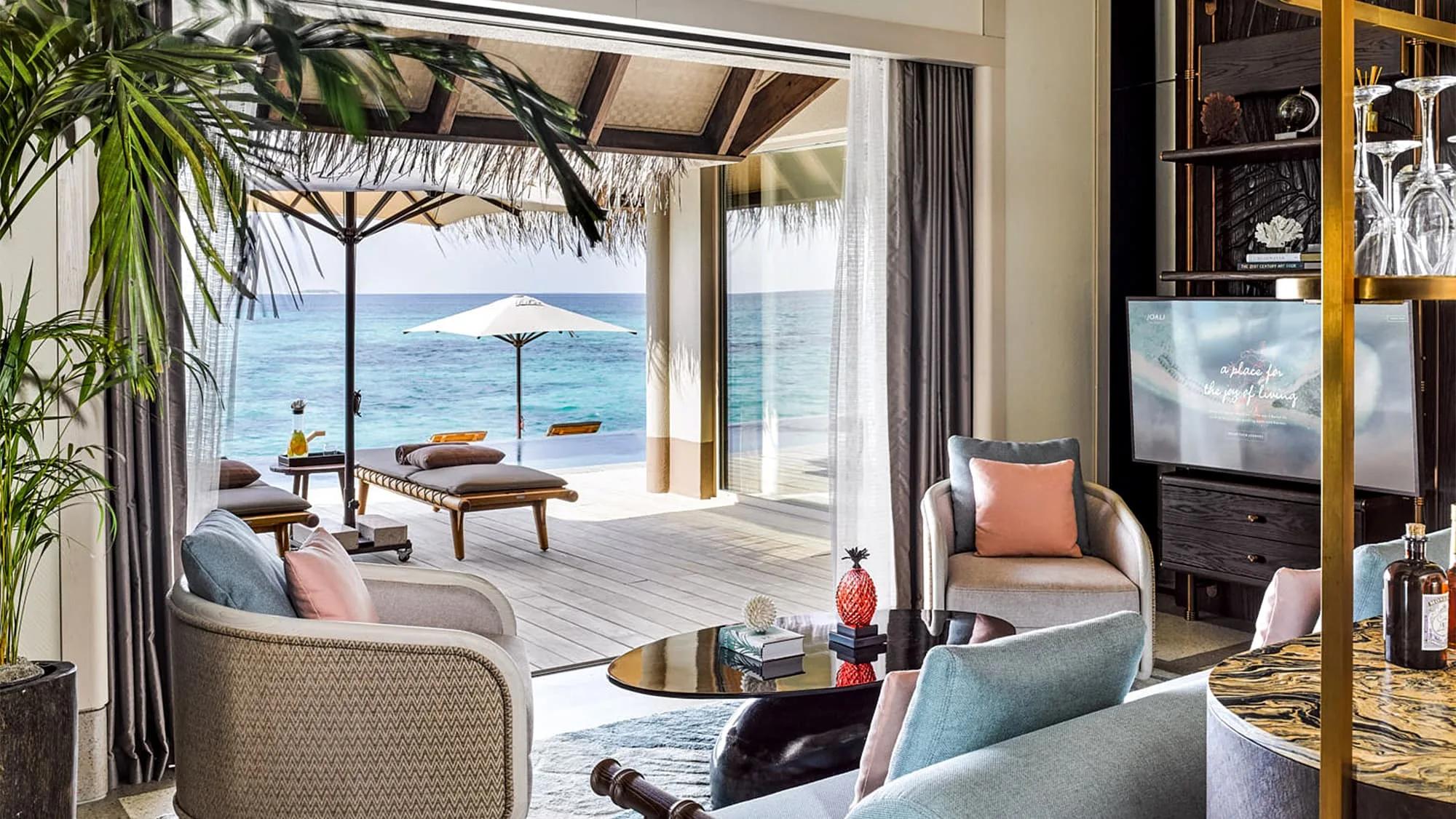 The living room of a Three Bedroom Ocean Residence with Two Pools, opening onto an overwater deck and infinity pool