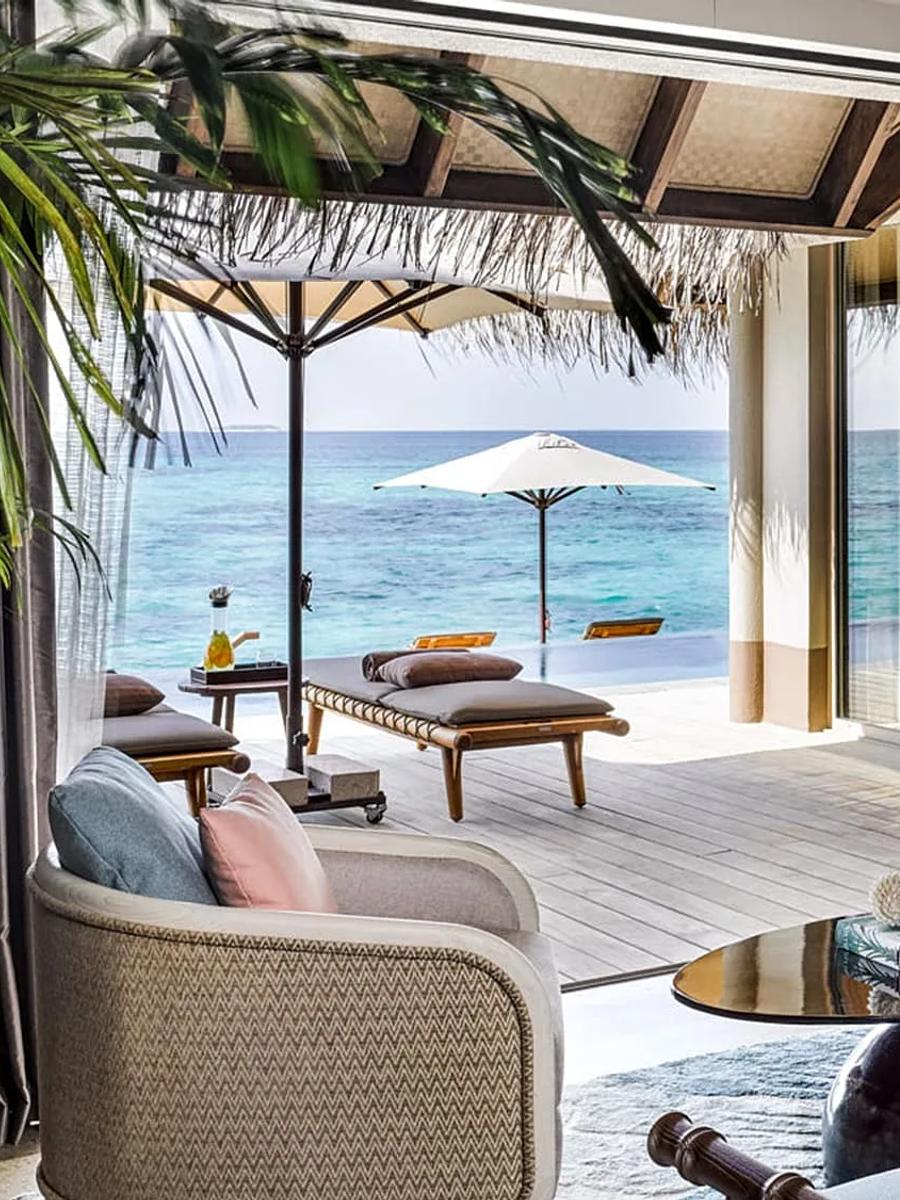 The living room of a Three Bedroom Ocean Residence with Two Pools, opening onto an overwater deck and infinity pool