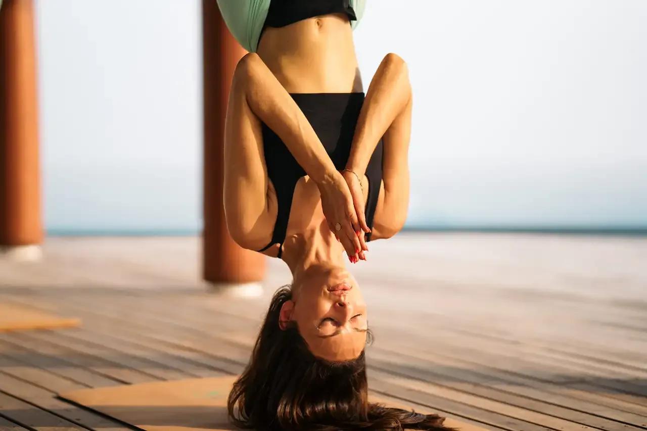 A guest practising an inversion pose on Meyyafushi's yoga deck, facing the lagoon