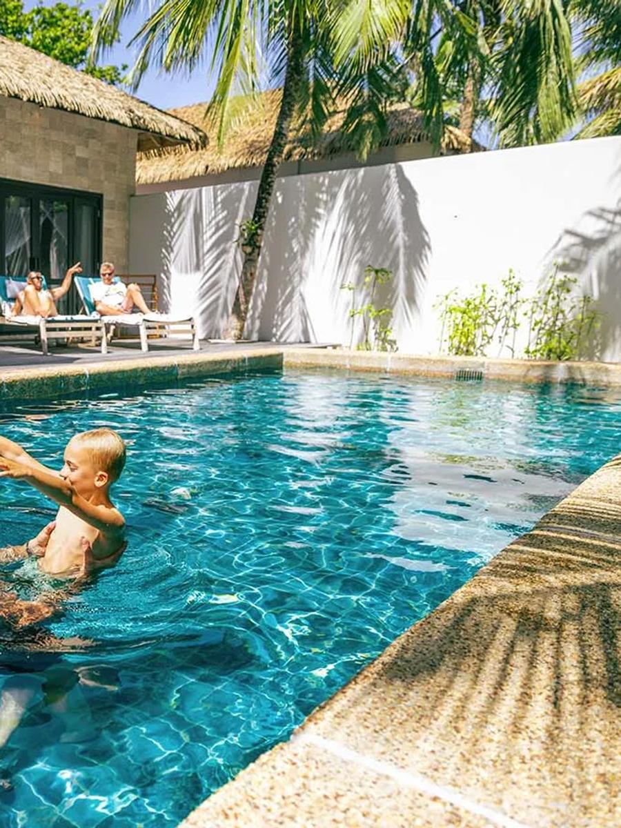 A family swimming together in a Private Pool Villa Family Suite's private pool, thatched roof behind