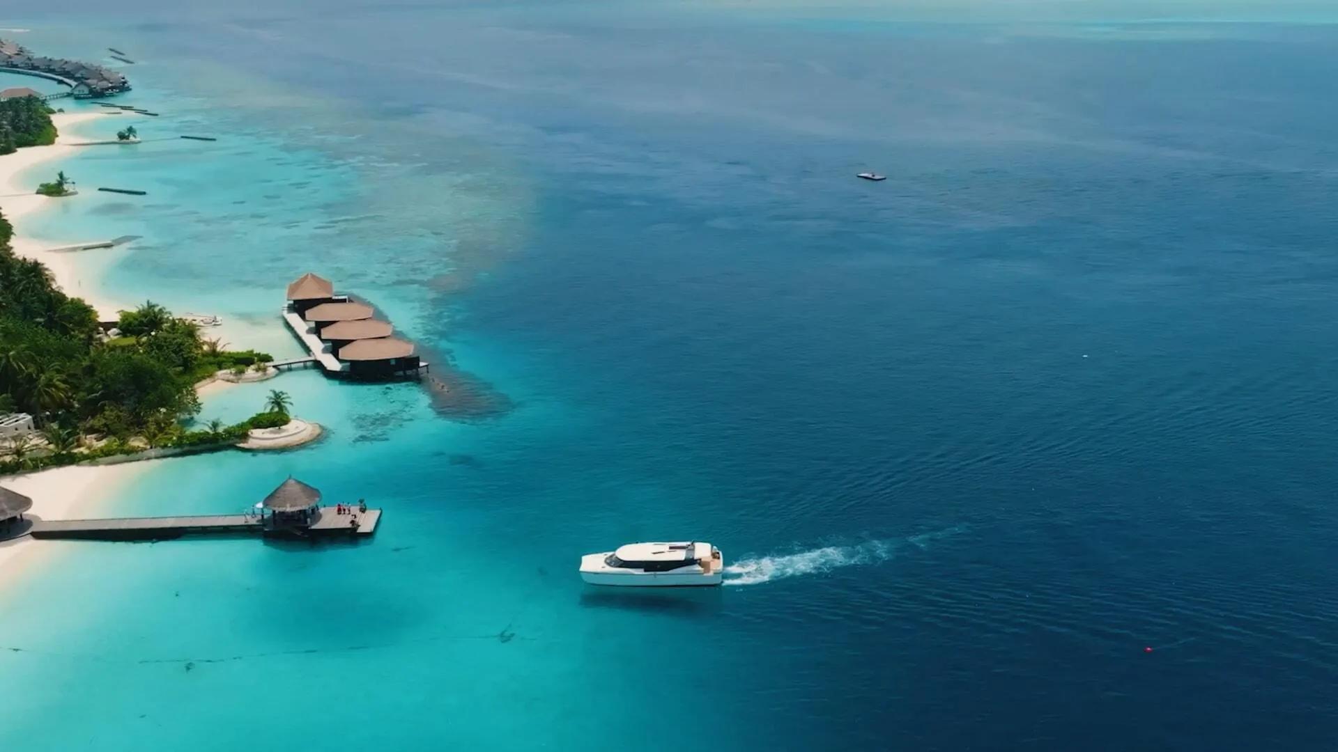A private catamaran approaching Bolifushi Island's overwater villas and jetty, its wake cutting across the turquoise lagoon