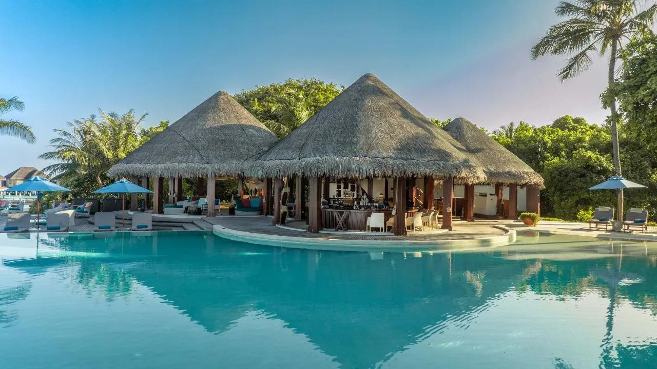 Sand Bar's thatched pool-bar structure at Dusit Thani Maldives, seen across the resort's infinity pool