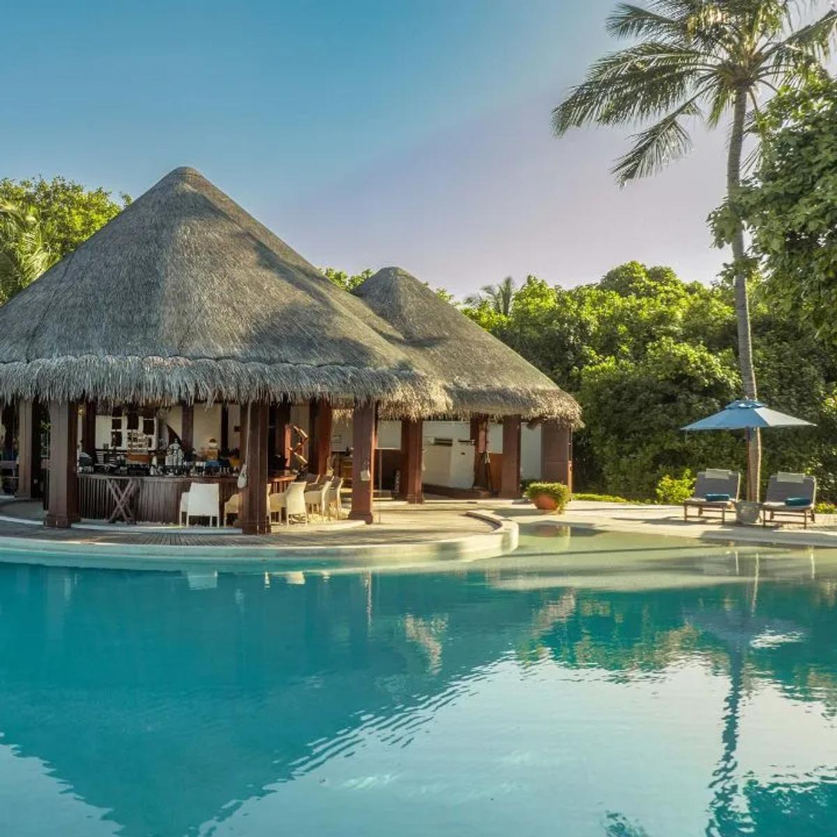 Sand Bar's thatched pool-bar structure at Dusit Thani Maldives, seen across the resort's infinity pool