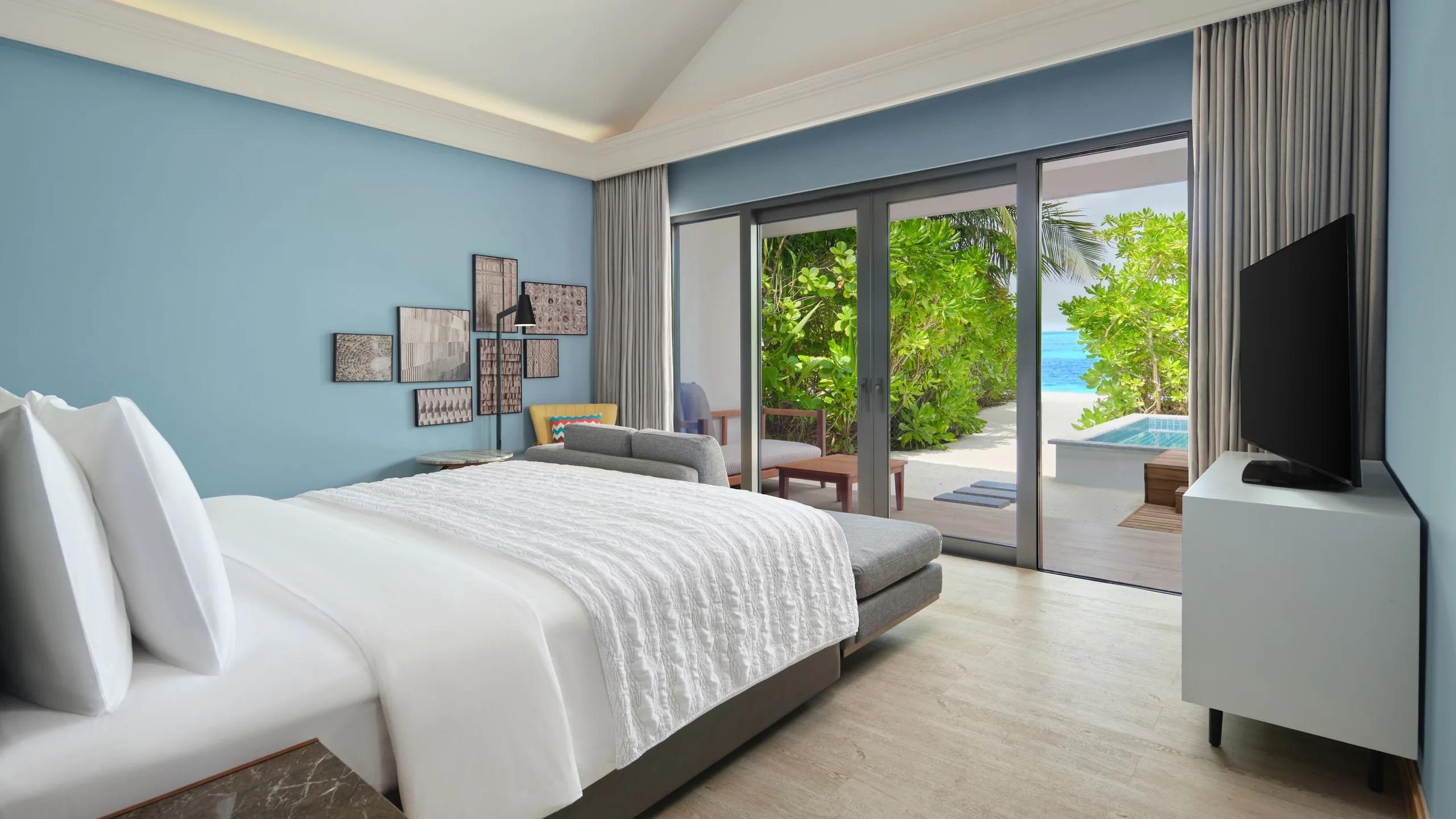 A bedroom inside a Beach Villa opening onto its pool deck at Le Méridien Maldives