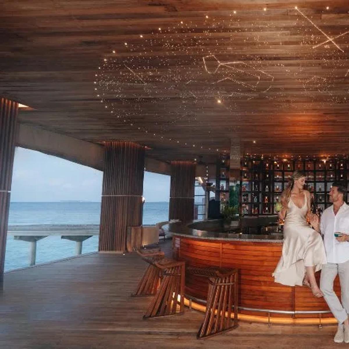 Guests seated at SKY, the overwater observatory lounge, Anantara Kihavah Maldives Villas
