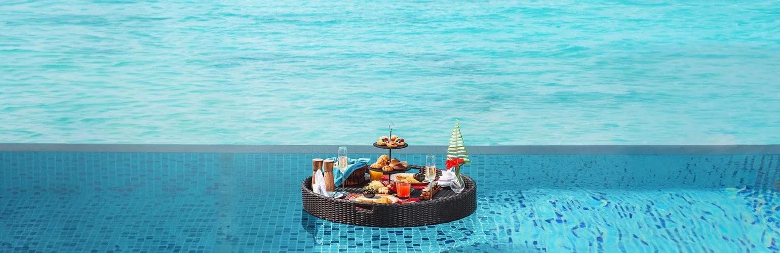 A floating breakfast tray of pastries and fruit set on the surface of an infinity pool