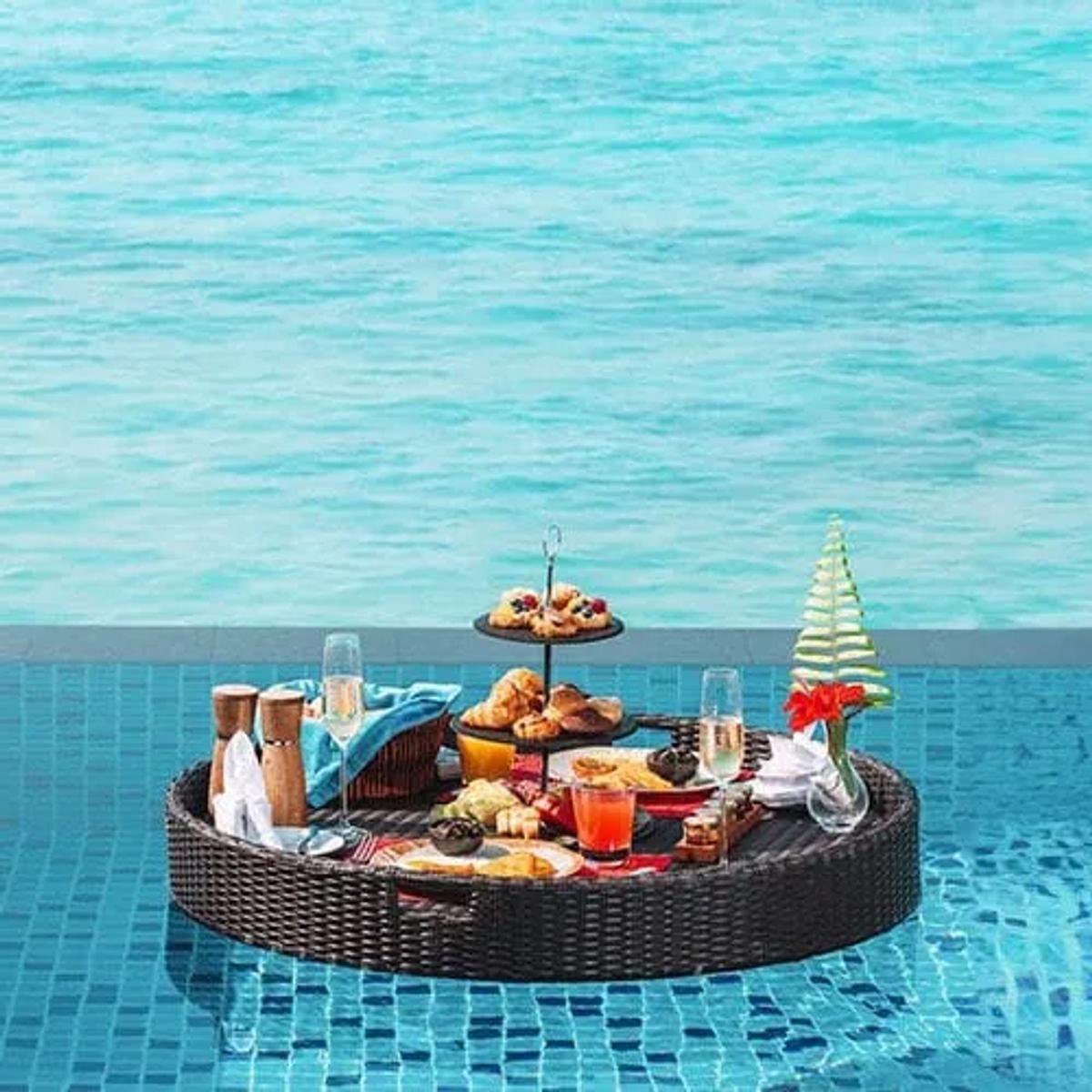 A floating breakfast tray of pastries and fruit set on the surface of an infinity pool