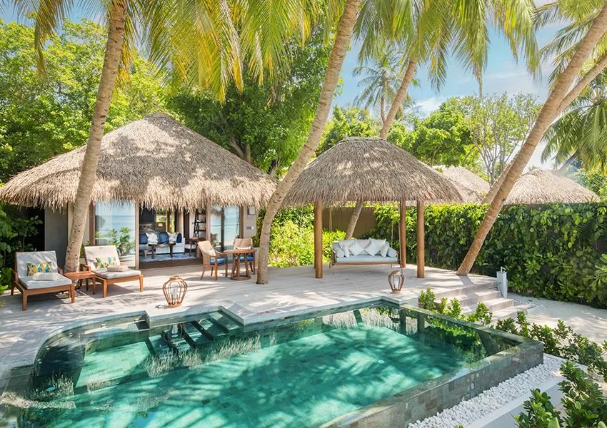 A Baros Suite's outdoor pool deck and shaded daybed swing under palm trees, with the open-plan living pavilion behind
