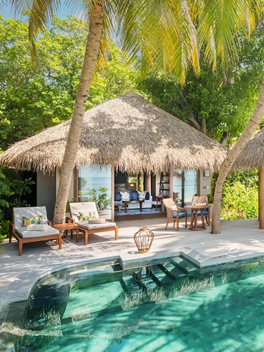A Baros Suite's outdoor pool deck and shaded daybed swing under palm trees, with the open-plan living pavilion behind