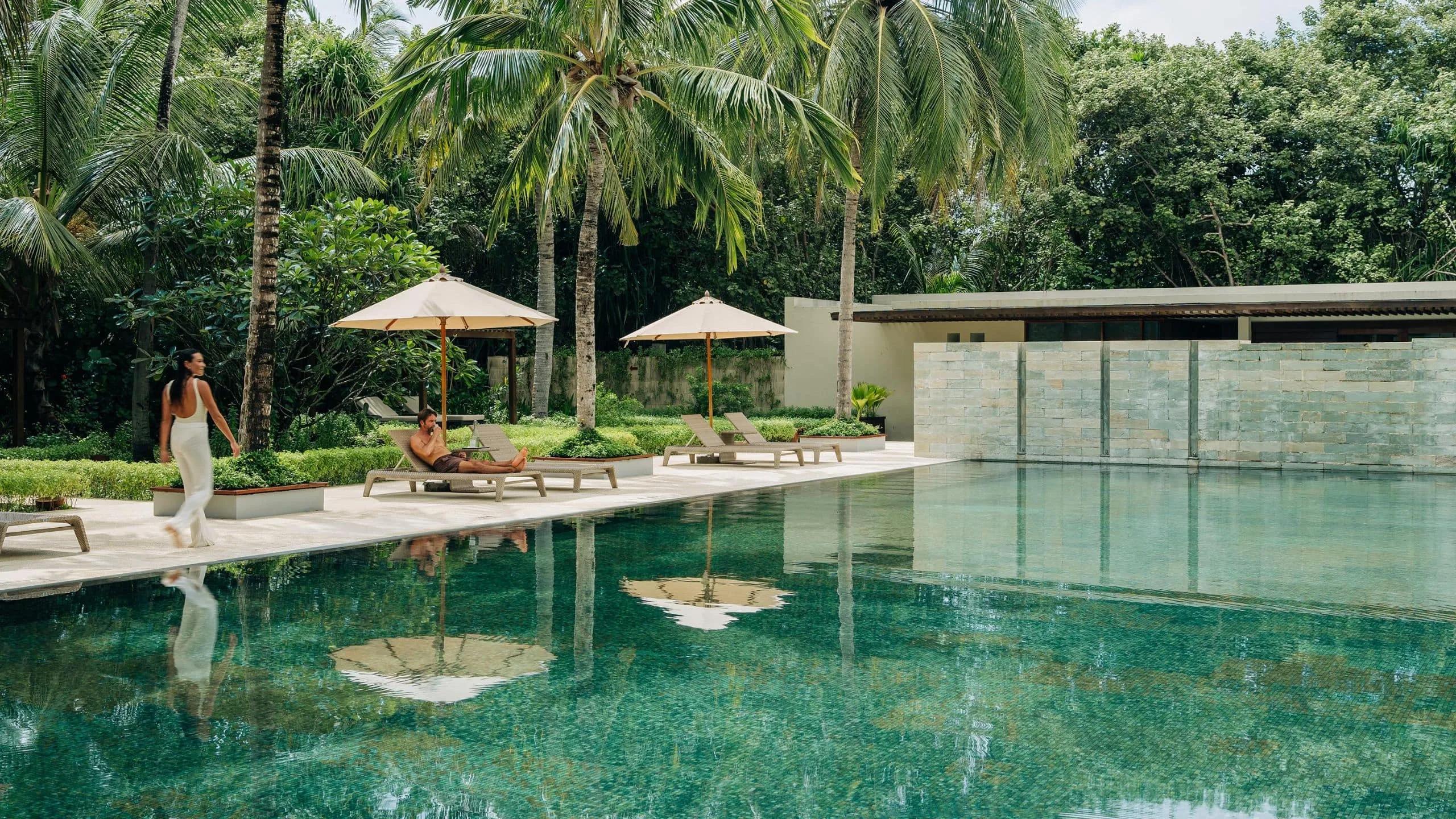 Guests beside the resort's main infinity pool, palm trees framing the deck