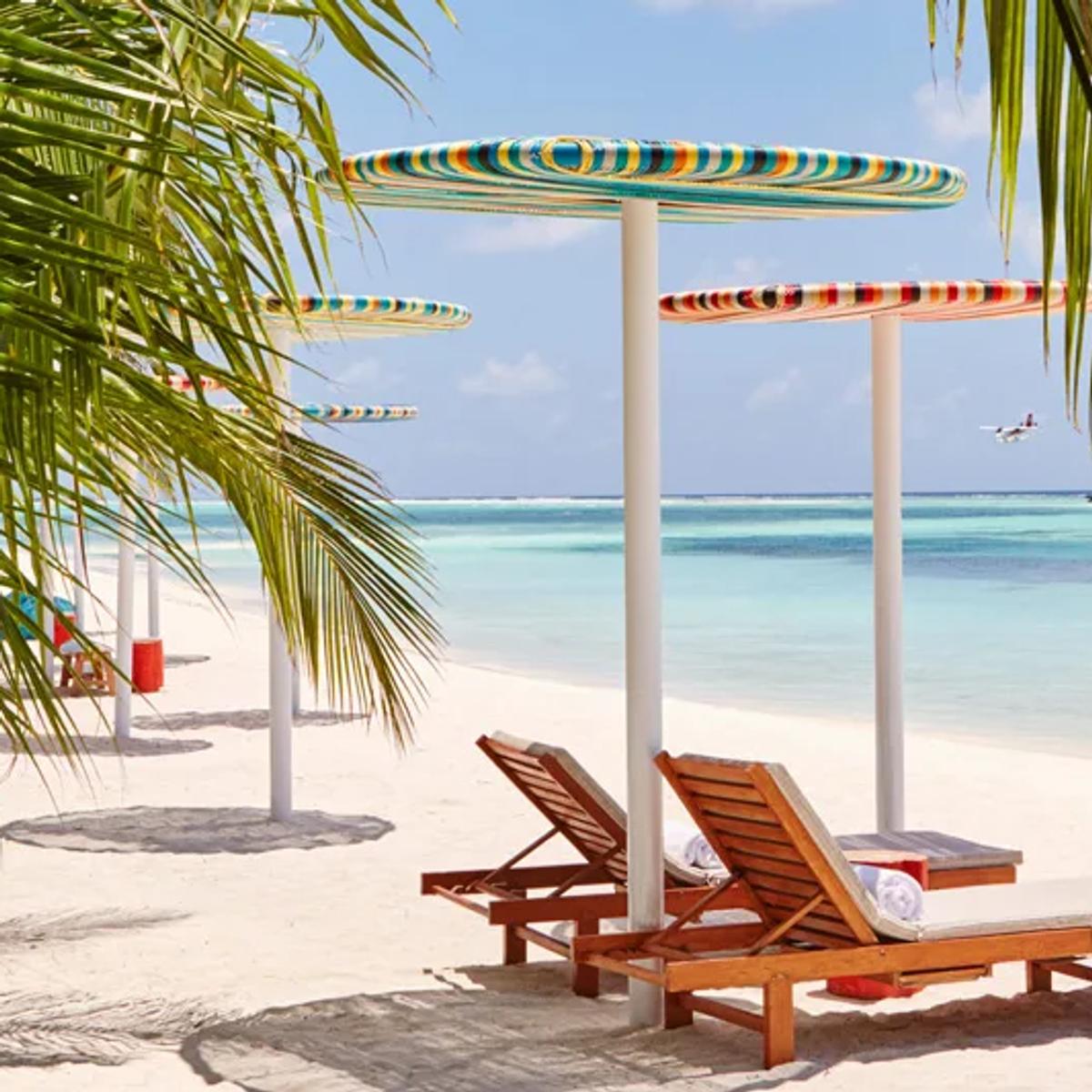 Striped umbrellas and wooden loungers on the beach, with the overwater villa row visible across the lagoon