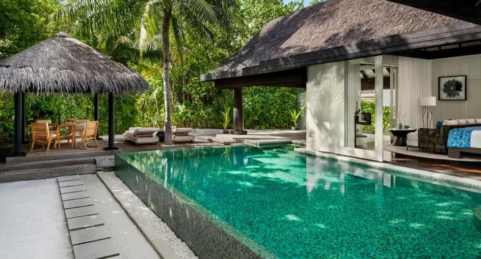 A thatched-roof pavilion and dining table beside a Beach House with Pool's infinity pool, palm trees framing the deck