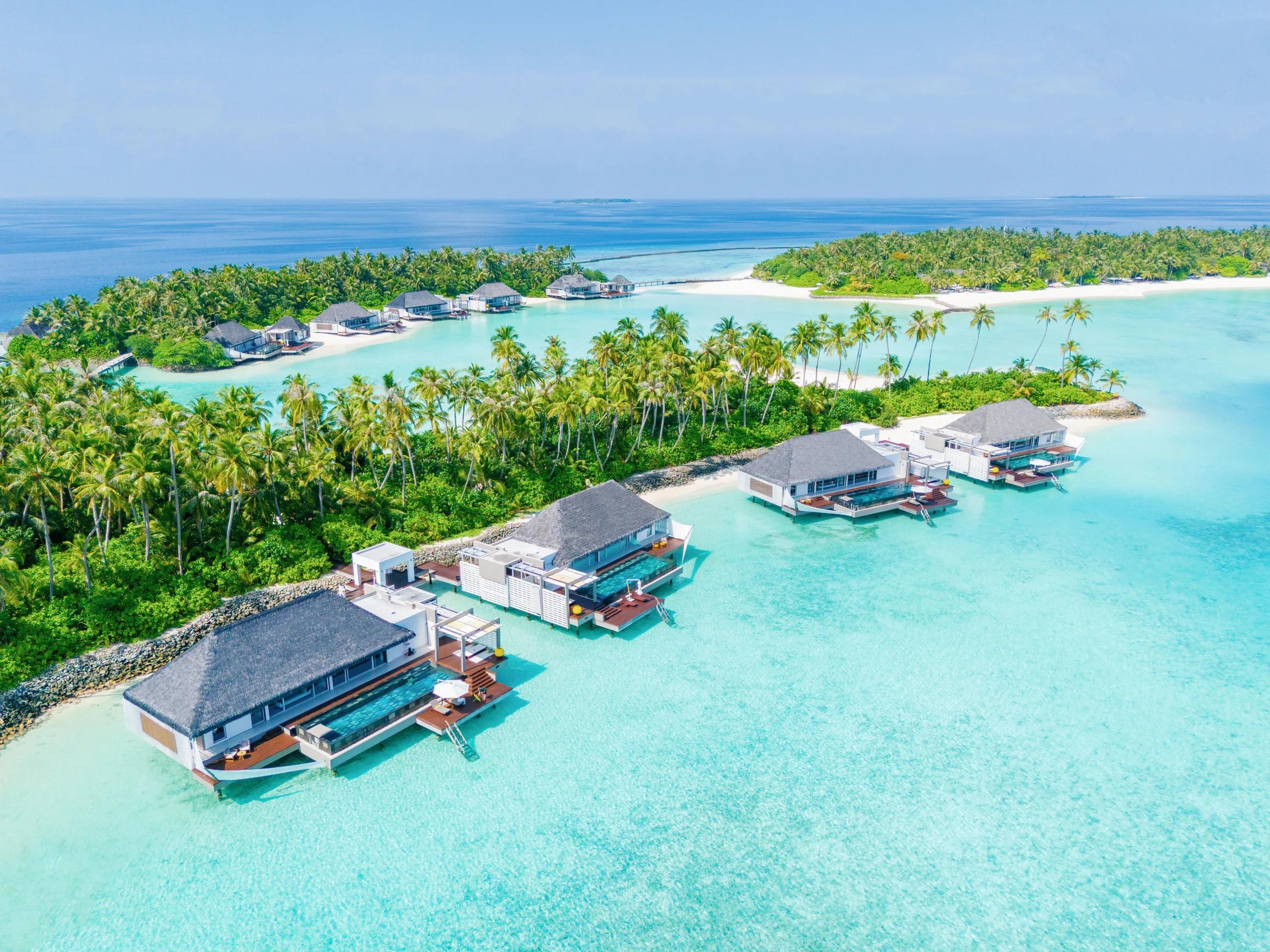 Golden-hour aerial view of Cheval Blanc Randheli's overwater villas extending from the beach into the lagoon