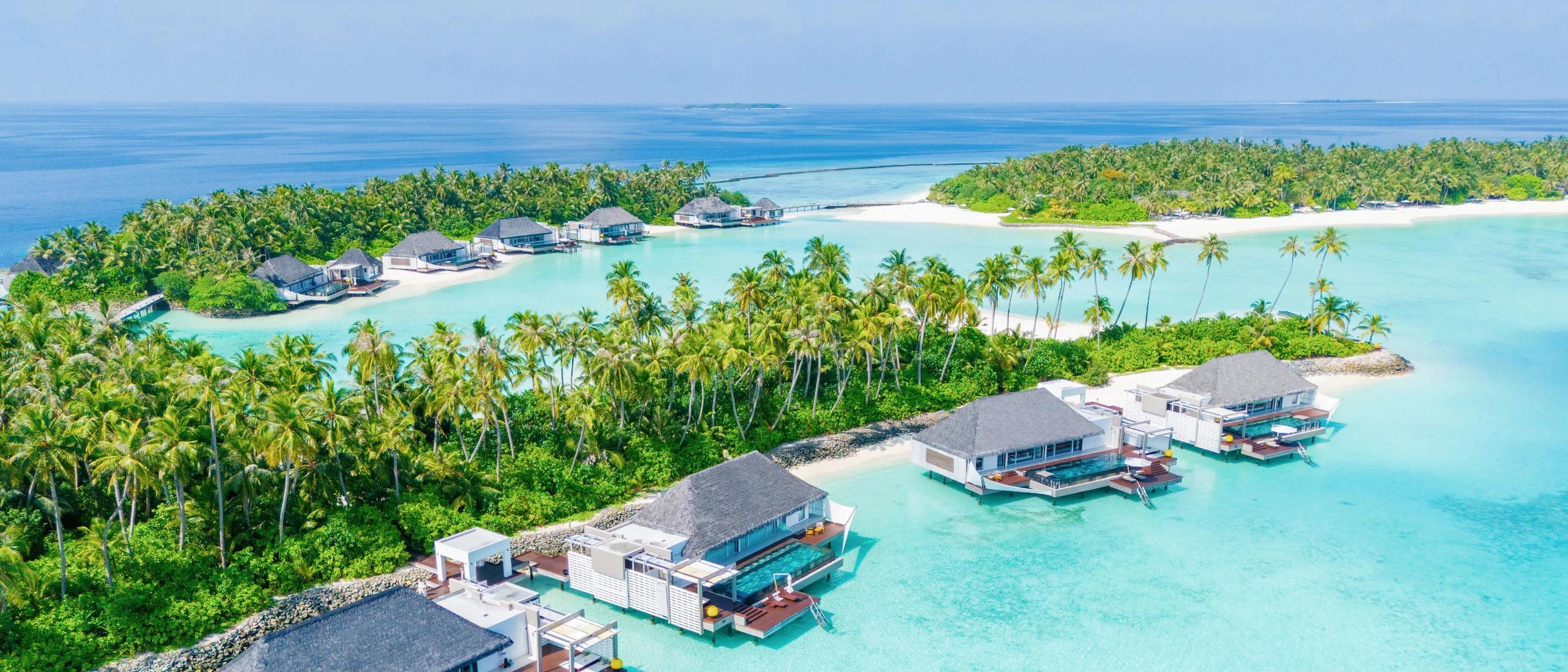 Golden-hour aerial view of Cheval Blanc Randheli's overwater villas extending from the beach into the lagoon