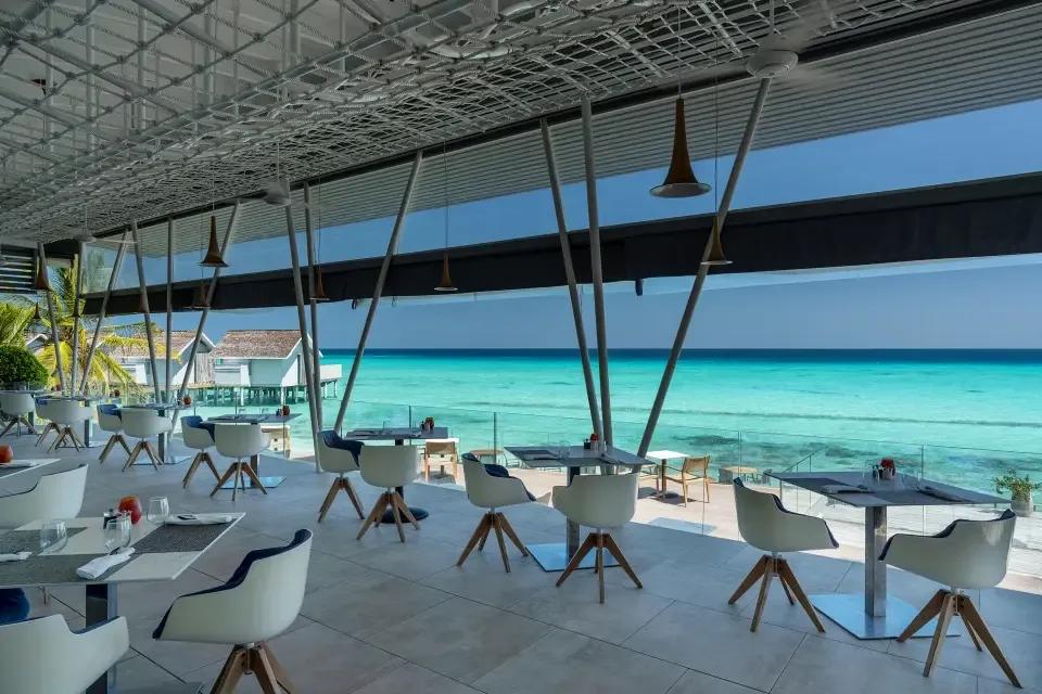 Inguru's glass-walled overwater deck with white swivel chairs facing the open lagoon