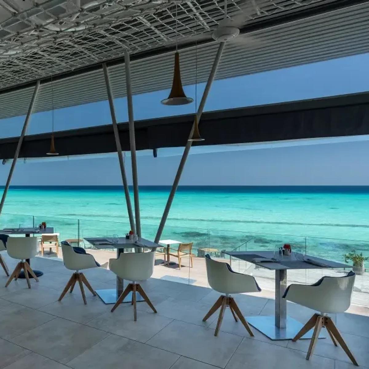 Inguru's glass-walled overwater deck with white swivel chairs facing the open lagoon