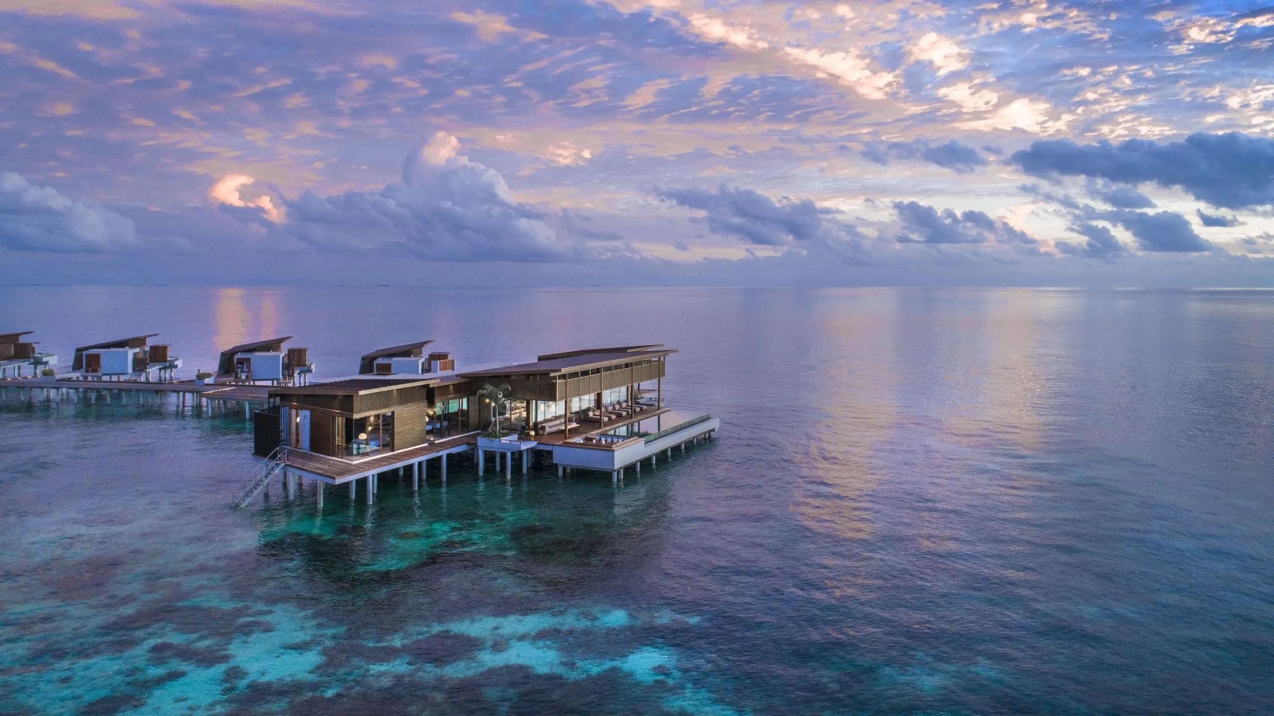 Overwater villas at Park Hyatt Maldives Hadahaa silhouetted against a dusk sky, seen from above the lagoon