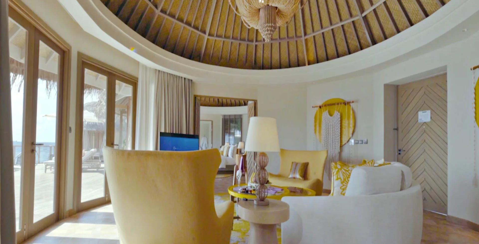 The Nautilus Retreat's sitting room in mustard tones, with a bedroom and overwater deck visible beyond.