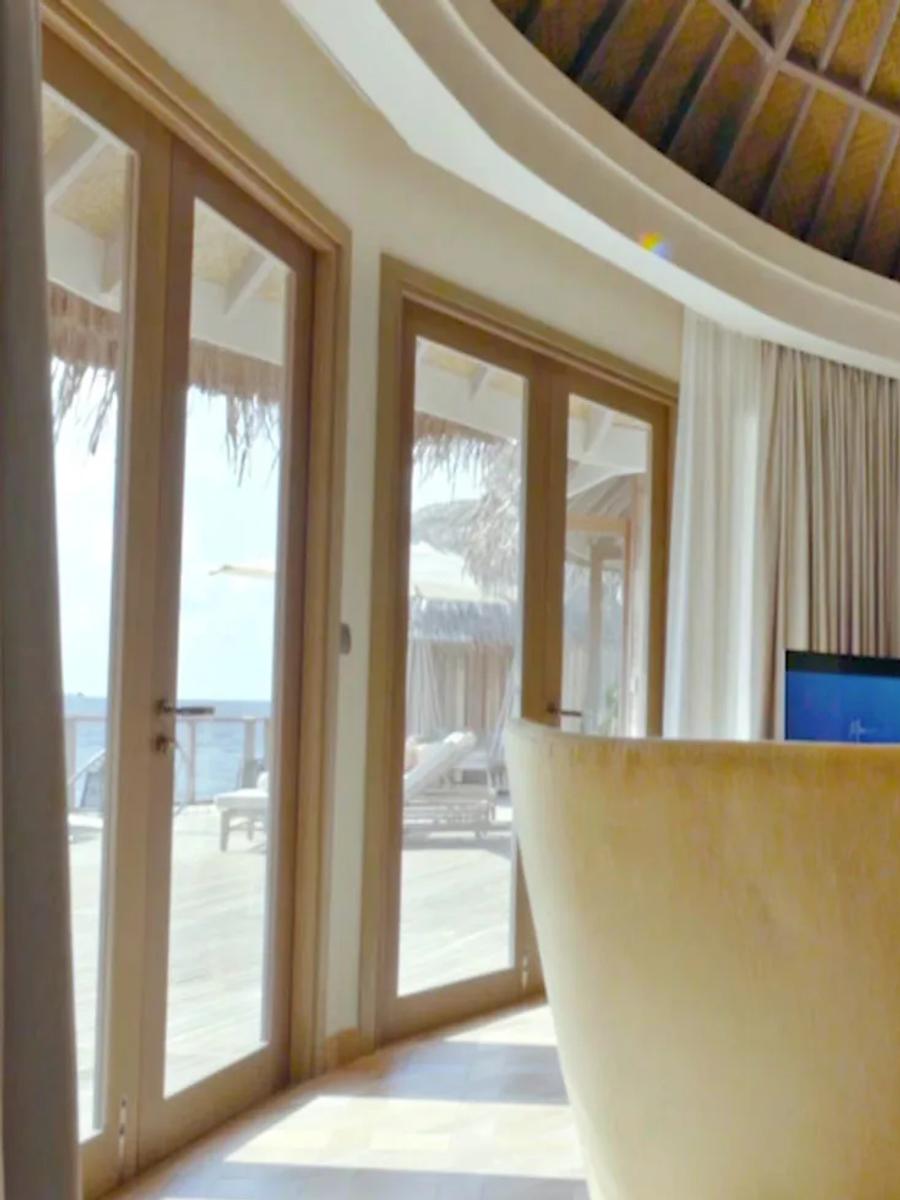 The Nautilus Retreat's sitting room in mustard tones, with a bedroom and overwater deck visible beyond.