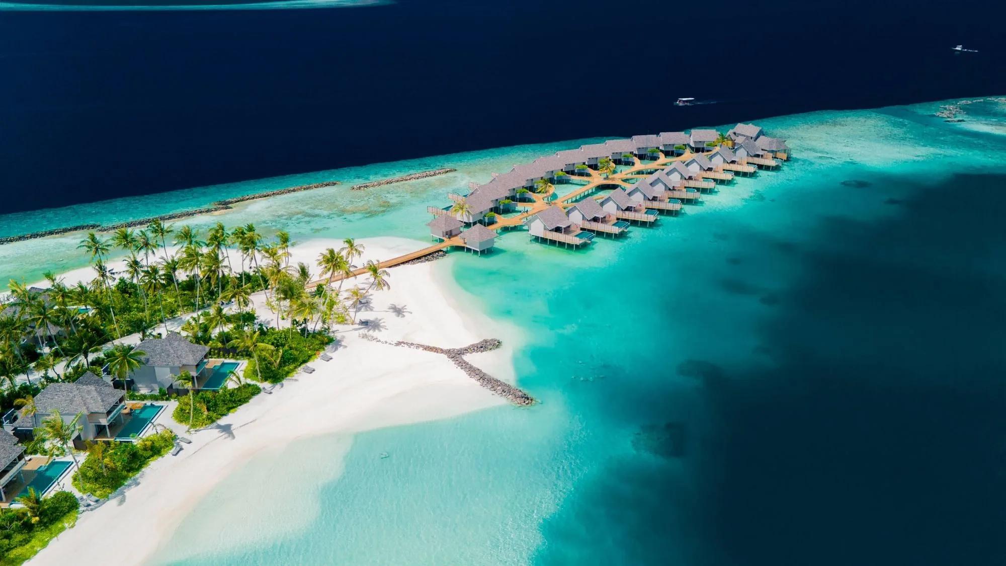 Aerial view of ananea Madivaru Maldives, overwater villas curving into the lagoon beside the beach villas and reef line