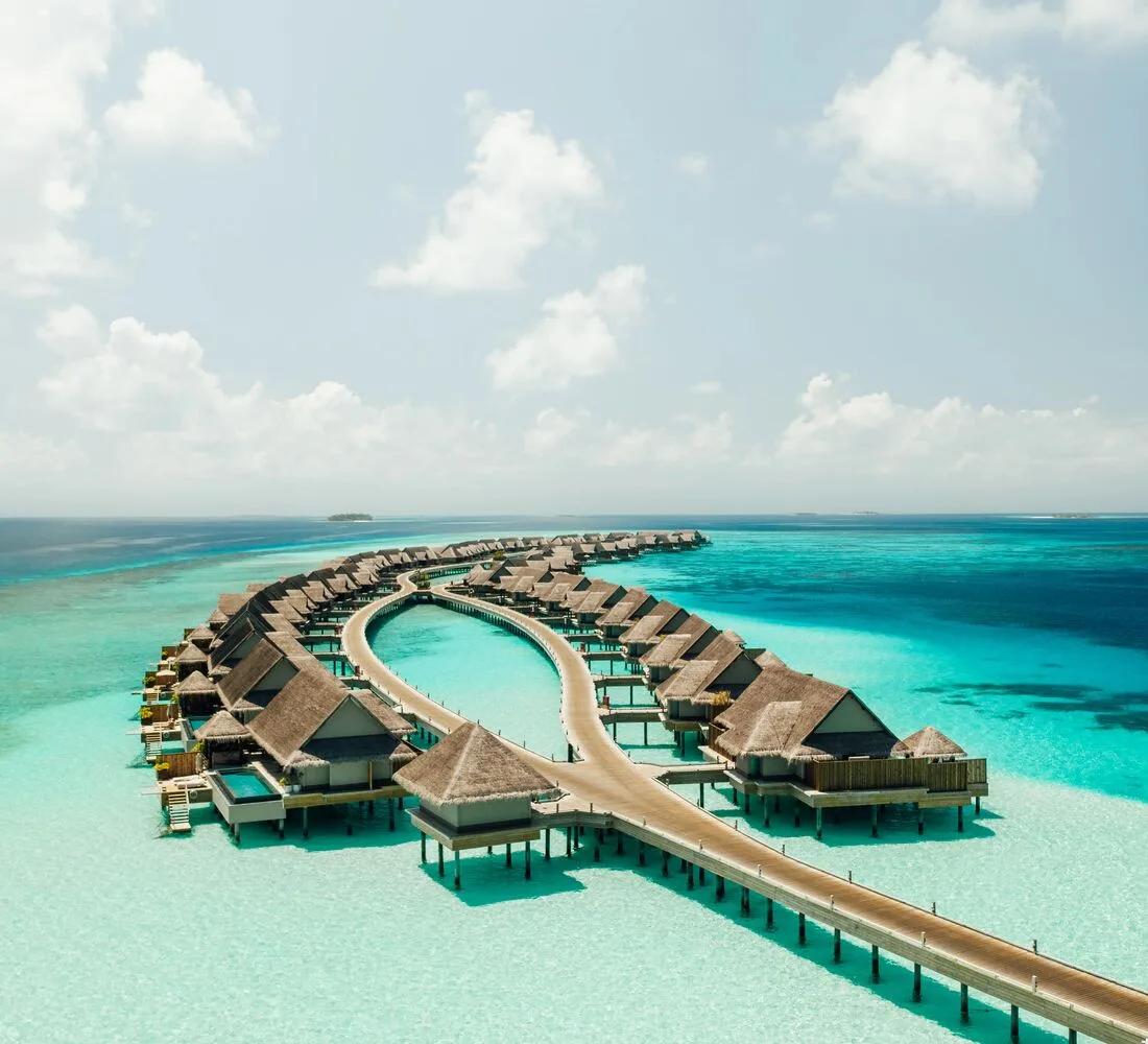 Aerial view of JOALI Maldives' overwater villas curving out from Muravandhoo Island across the turquoise lagoon