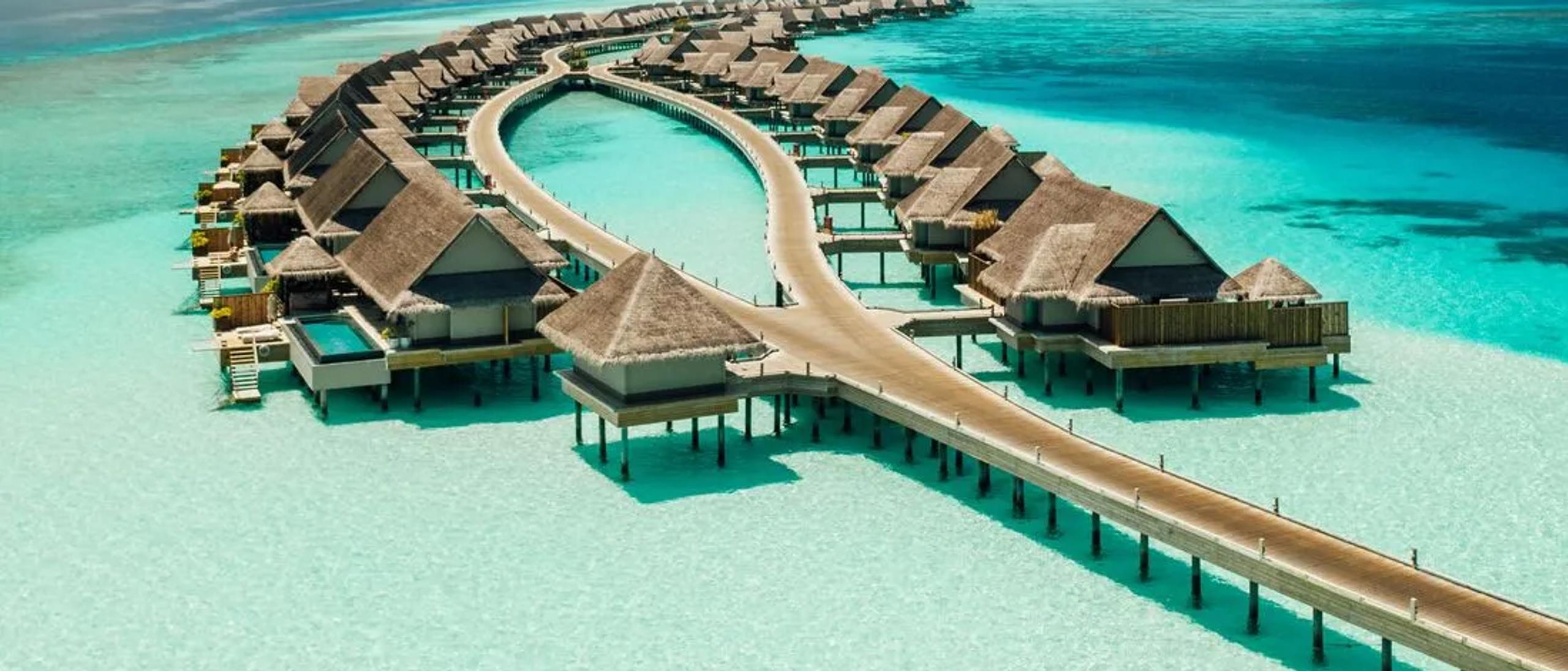 Aerial view of JOALI Maldives' overwater villas curving out from Muravandhoo Island across the turquoise lagoon