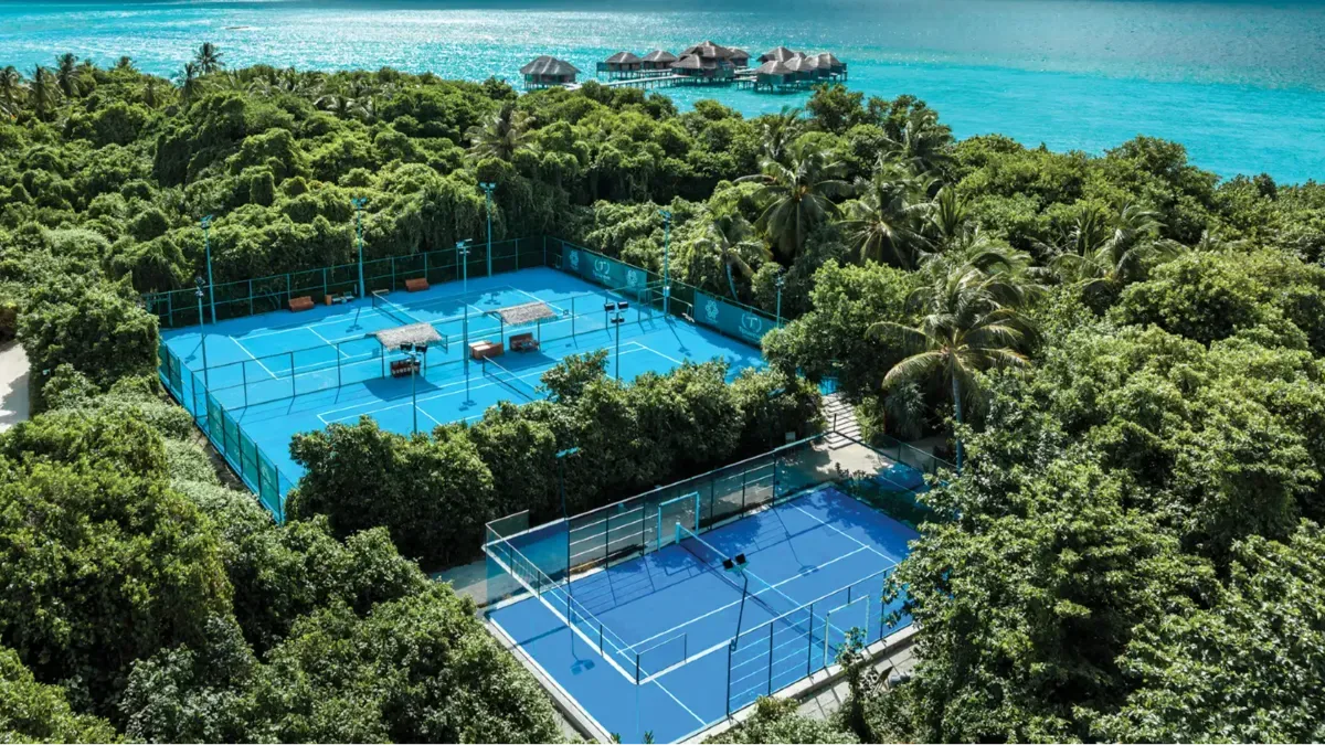 Aerial view of Vakkaru's tennis and padel courts cut into the jungle, overwater villas and open lagoon visible beyond