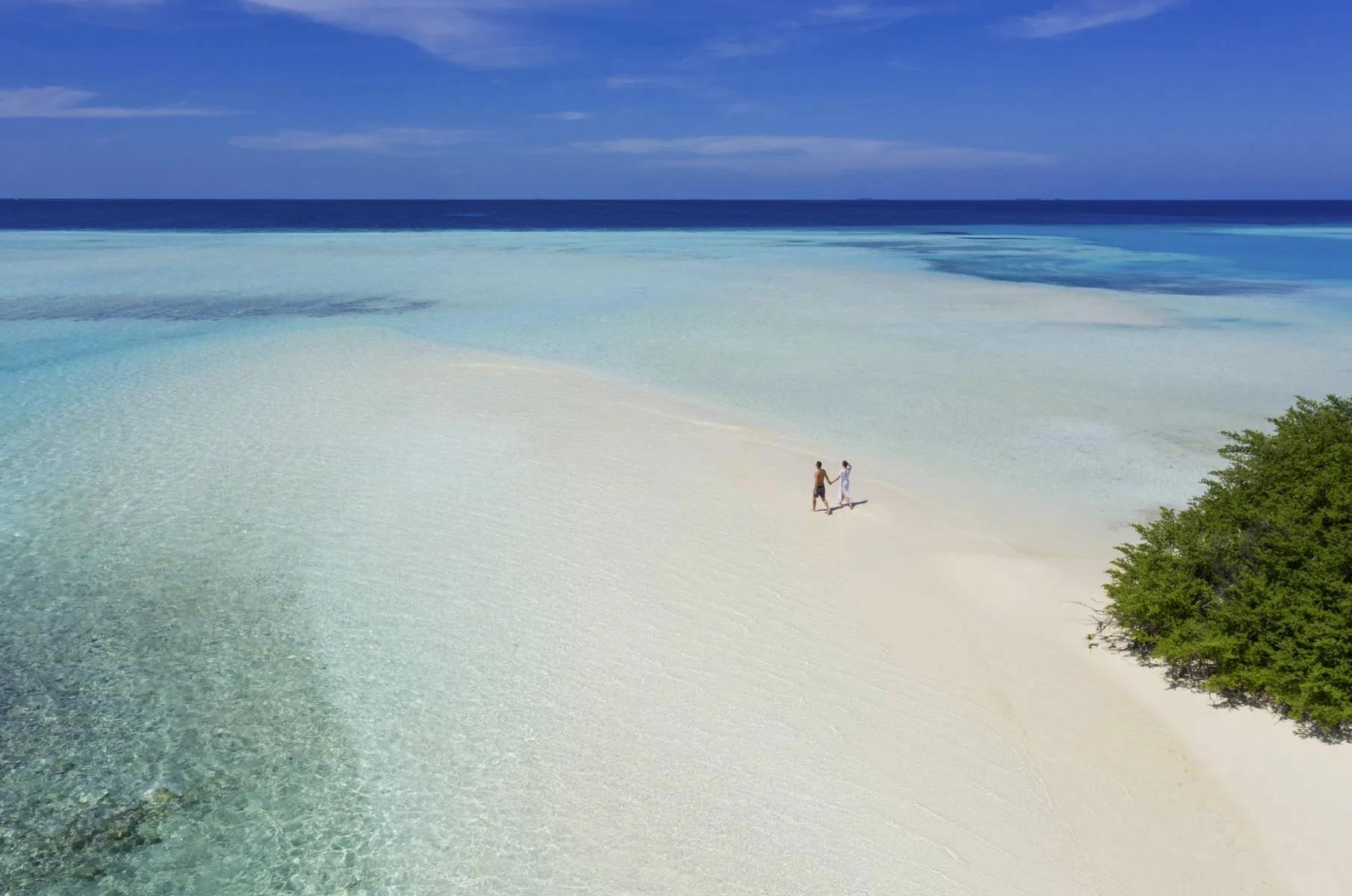 A couple standing on a sandbank in shallow turquoise water near the resort