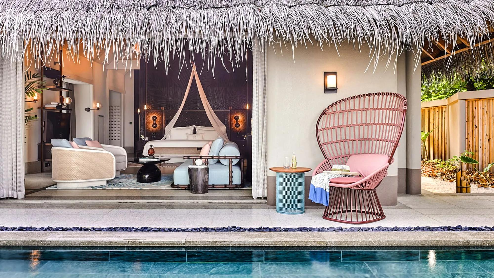 A Beach Villa's thatched-roof pool deck, with a woven rattan chair beside the pool and the bedroom visible through the open wall