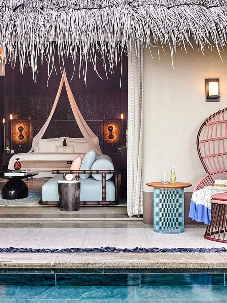A Beach Villa's thatched-roof pool deck, with a woven rattan chair beside the pool and the bedroom visible through the open wall