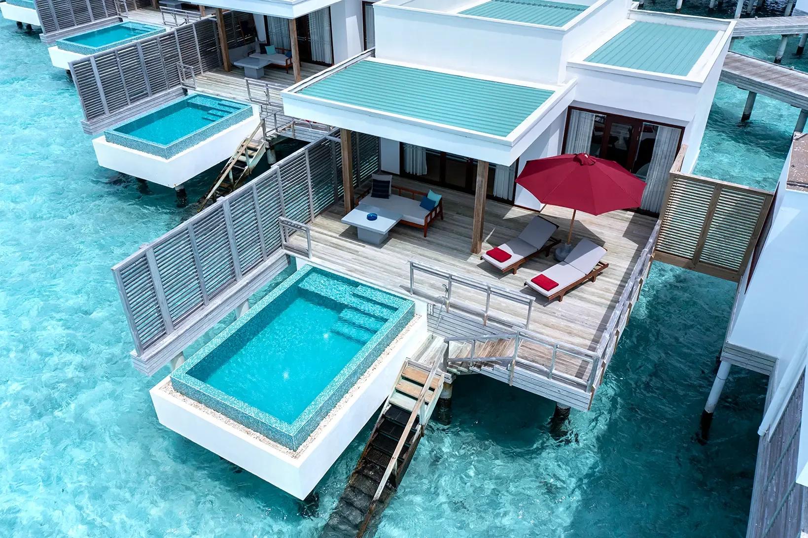 Aerial view of overwater villa decks and private plunge pools set directly over the lagoon at Niva Dhigali