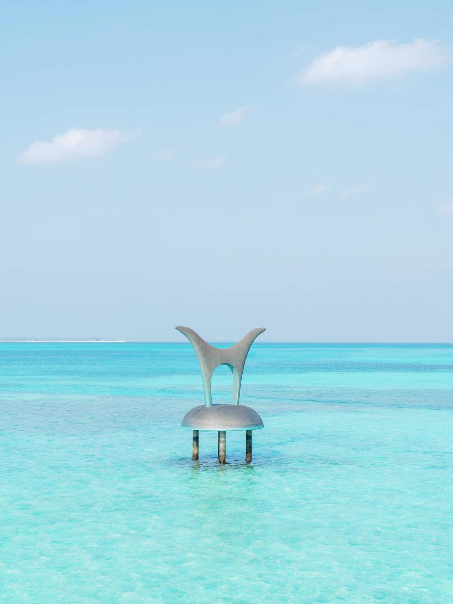 Vincent Beaurin's sculpture 'Arch' standing in shallow lagoon water near the resort's jetty