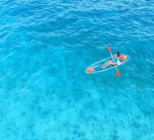 A guest paddling a clear-bottomed kayak over JOALI's shallow reef flats, seen from above