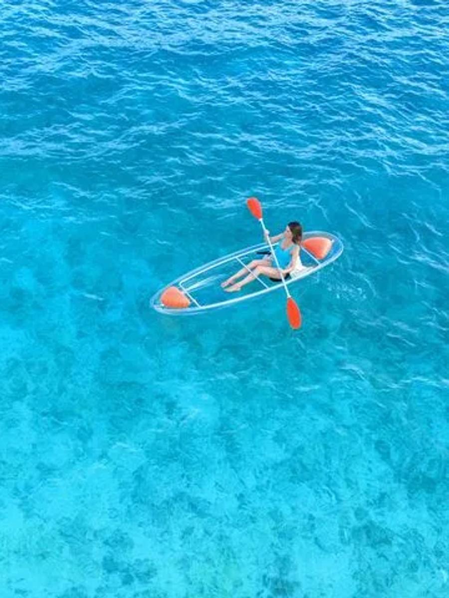 A guest paddling a clear-bottomed kayak over JOALI's shallow reef flats, seen from above