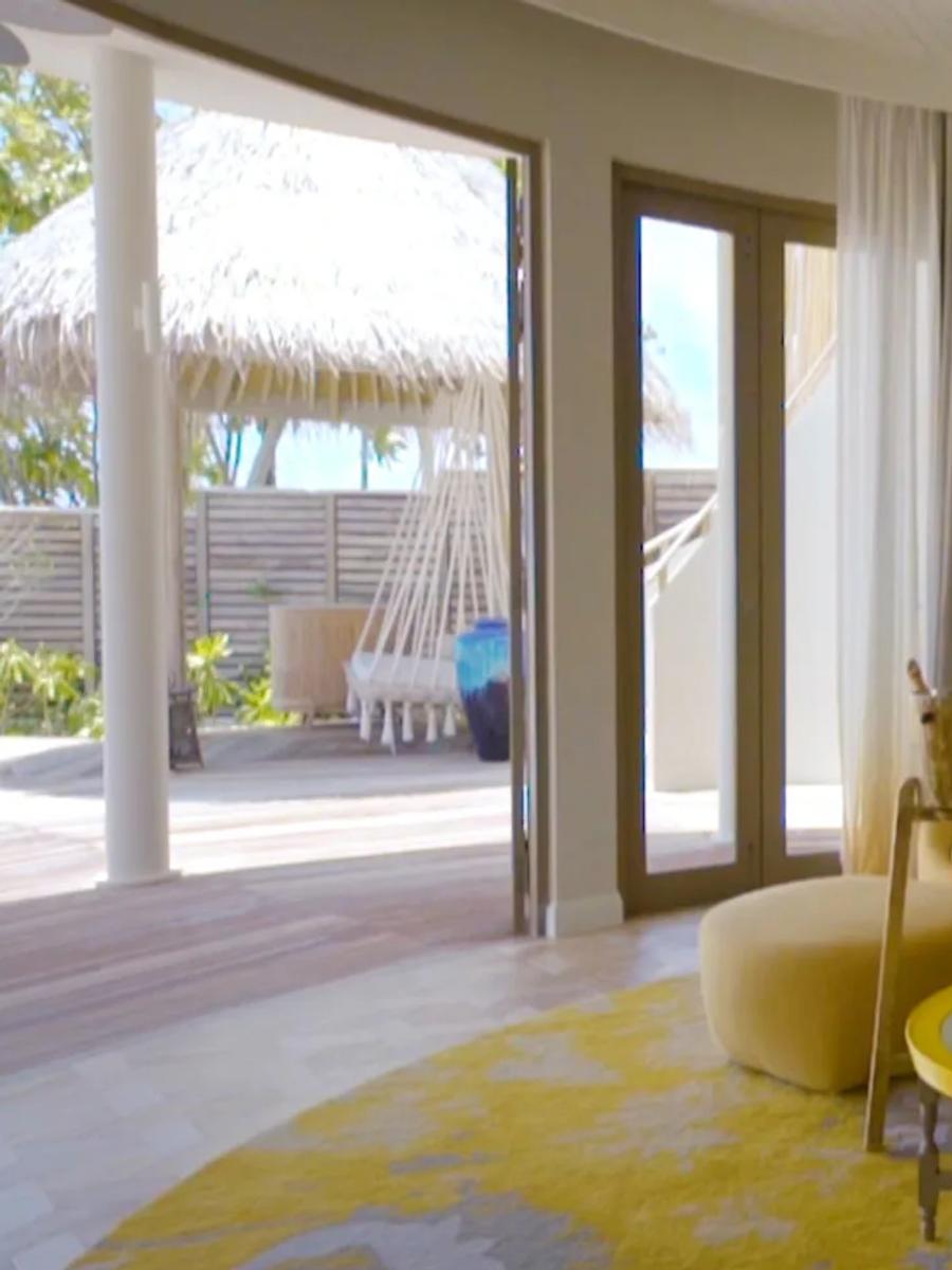 A Beach Residence living room in warm orange tones, a hammock visible on the deck outside.