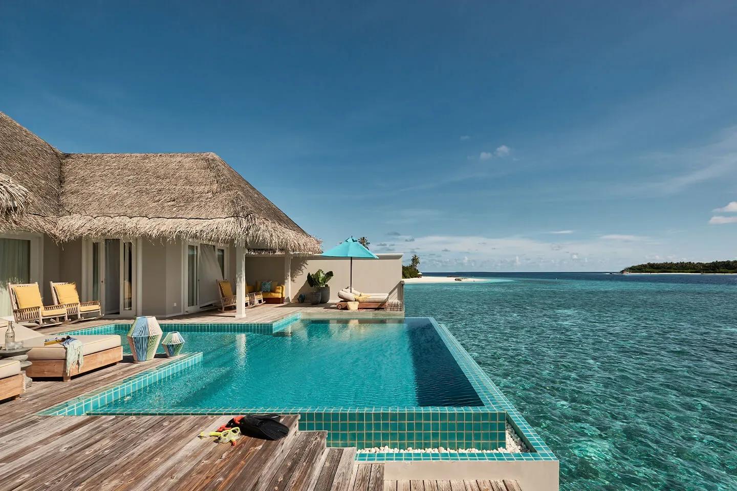 A Two Bedroom Water Villa's overwater deck, its private pool appearing to merge with the lagoon, a sandbank visible in the distance