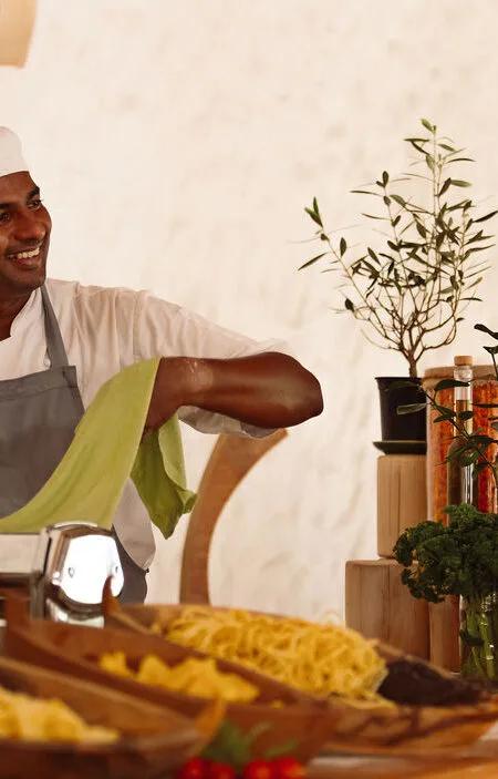 A chef at the Pasta Counter's open kitchen, trays of handmade pasta laid out beside fresh herbs and oils