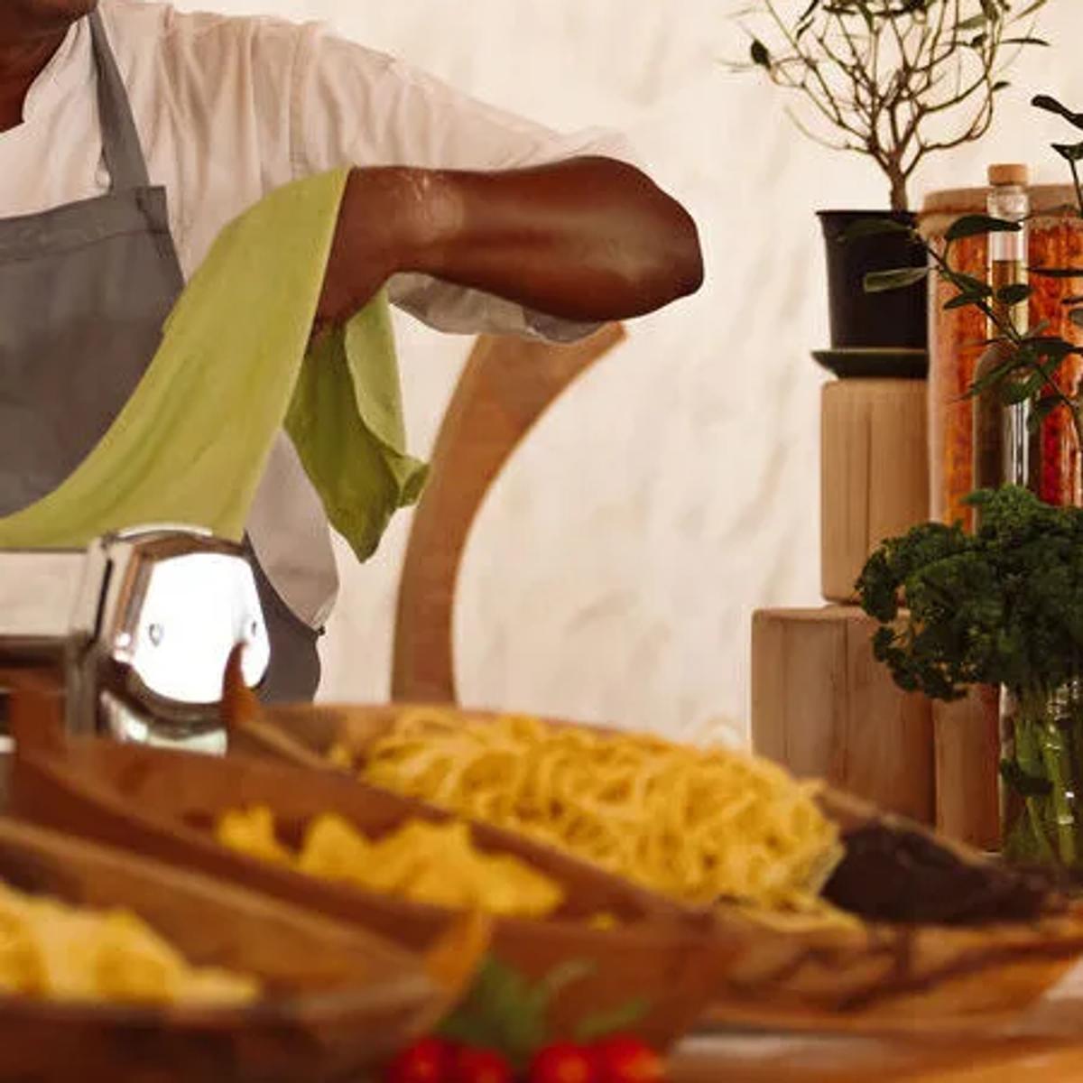 A chef at the Pasta Counter's open kitchen, trays of handmade pasta laid out beside fresh herbs and oils