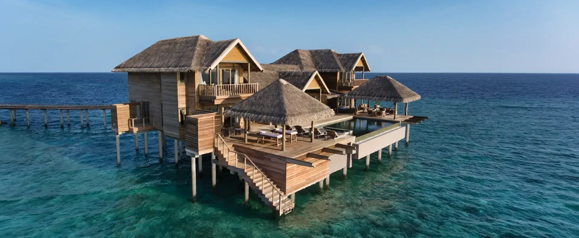 Aerial view of the Vakkaru Over Water Residence, its multiple thatched pavilions and pool built out over the reef