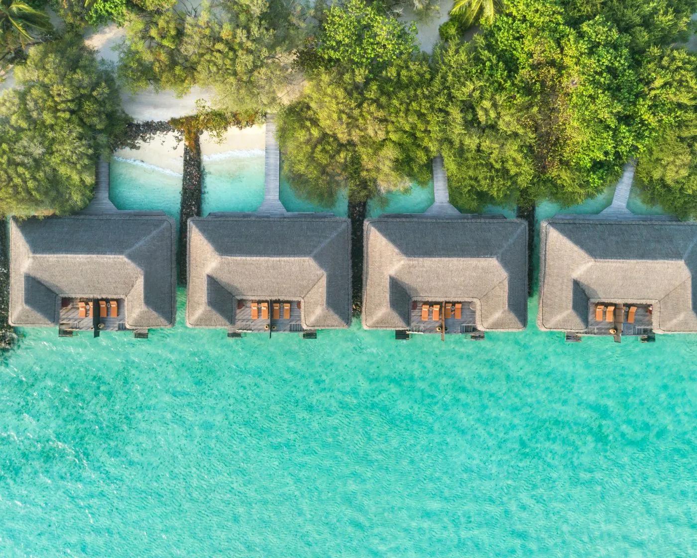 A row of Sunrise Overwater Villas seen from directly above, thatched roofs reaching out over the turquoise lagoon