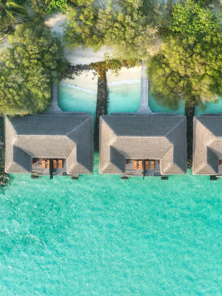 A row of Sunrise Overwater Villas seen from directly above, thatched roofs reaching out over the turquoise lagoon