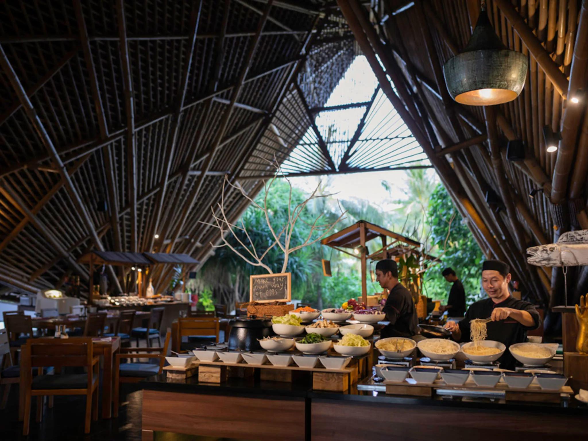 Chefs preparing noodles at ONU Marché's live cooking station, bowls of fresh vegetables and garnishes laid out under the restaurant's bamboo roof