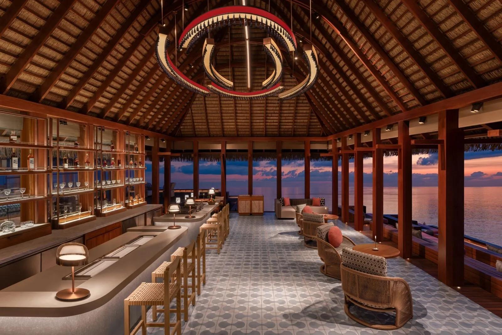 SIP, W Maldives' overwater cocktail bar, its bar and lounge seating lit for the evening as the sky turns pink over the ocean