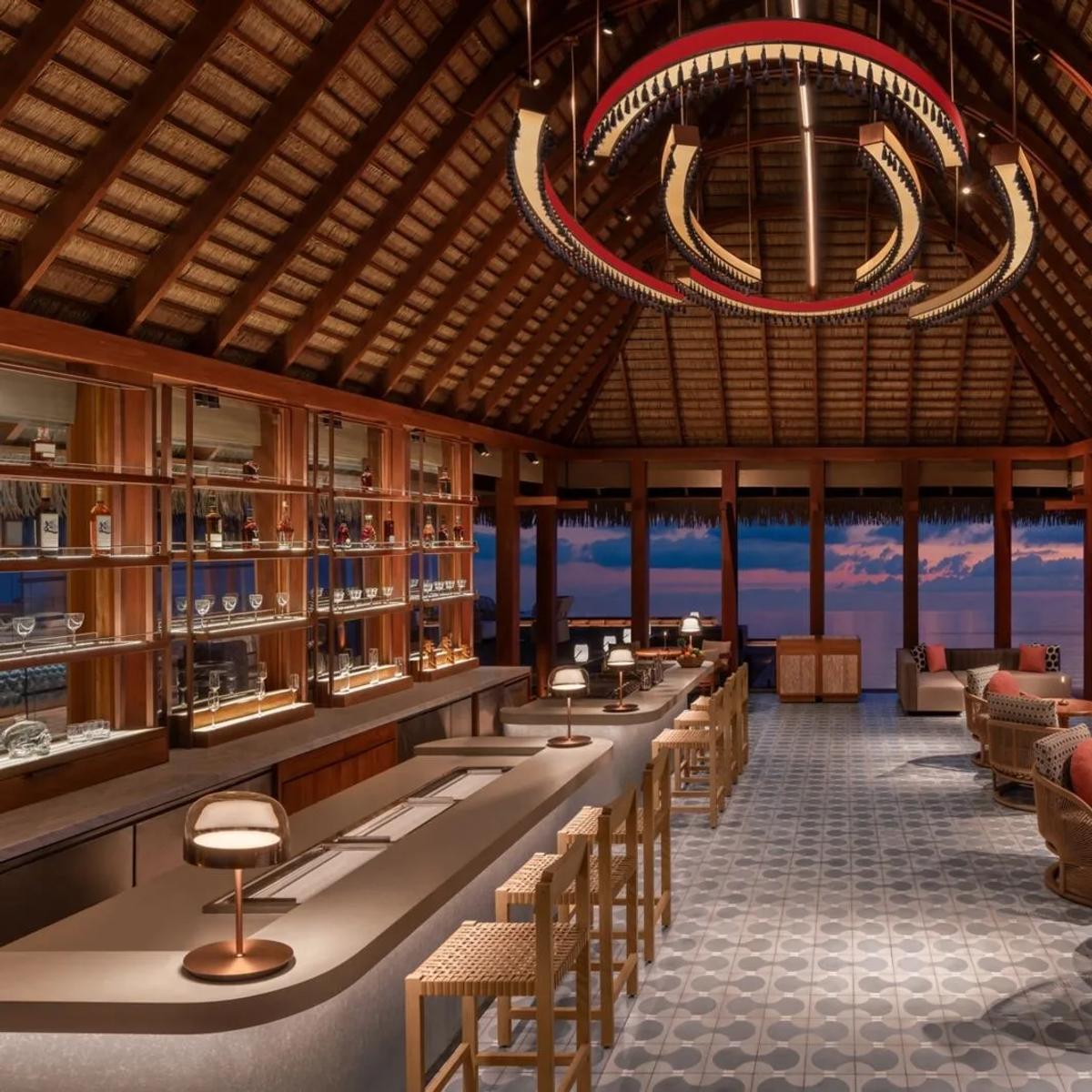 SIP, W Maldives' overwater cocktail bar, its bar and lounge seating lit for the evening as the sky turns pink over the ocean