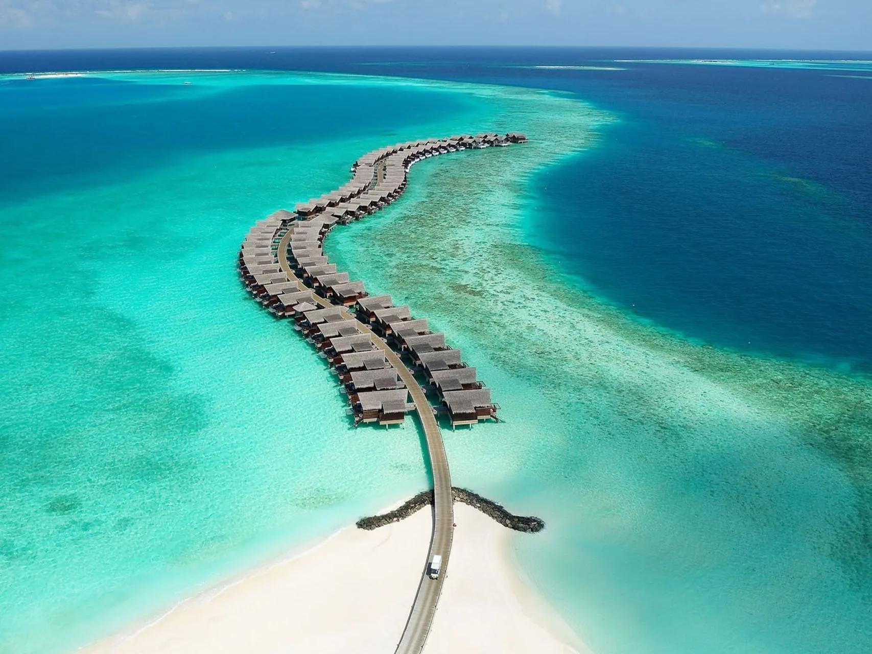 An aerial view of Grand Park Kodhipparu's island exterior, overwater villas fringing the reef