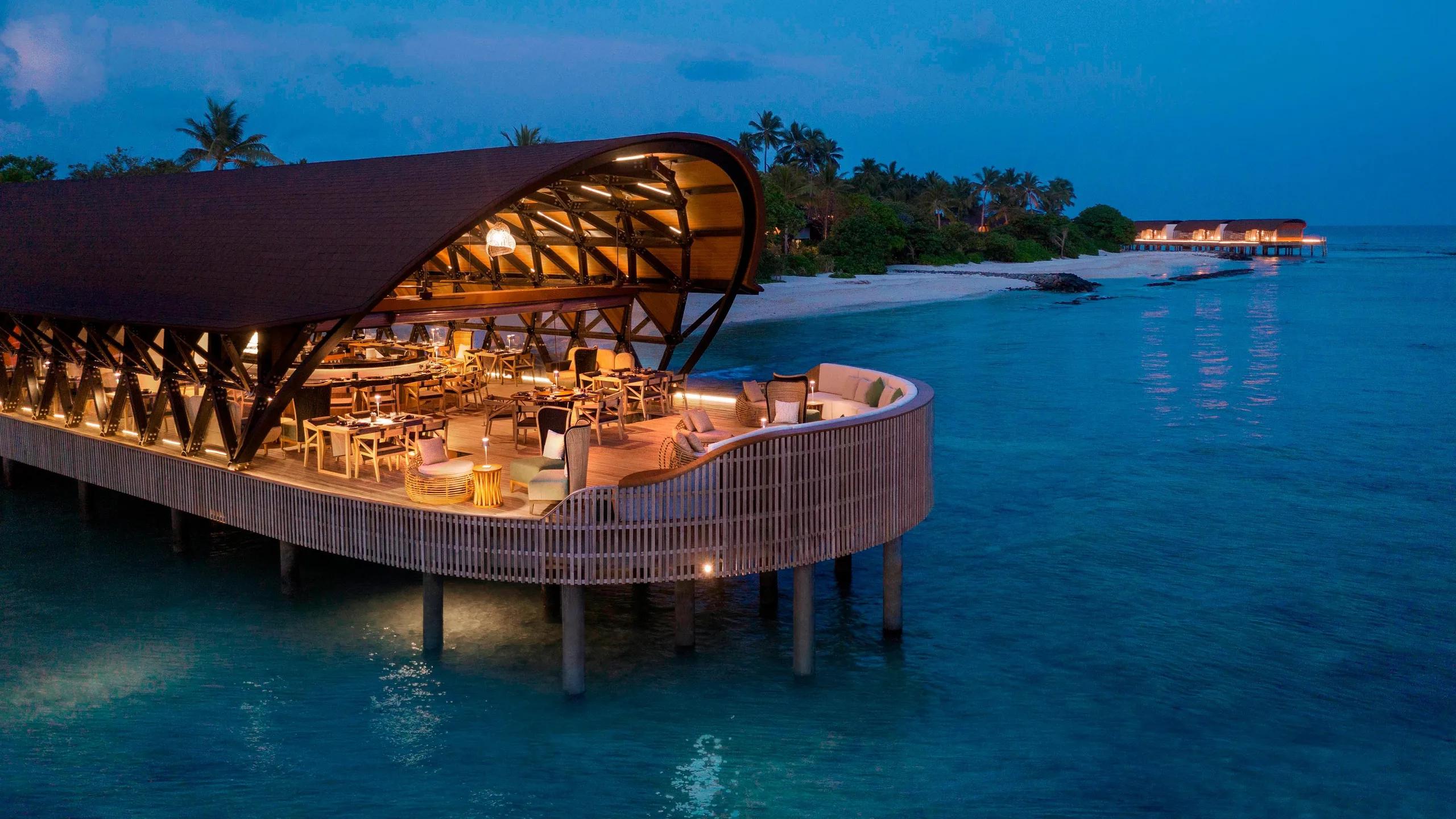 The resort's overwater dining pavilion at dusk, beach and jetty beyond