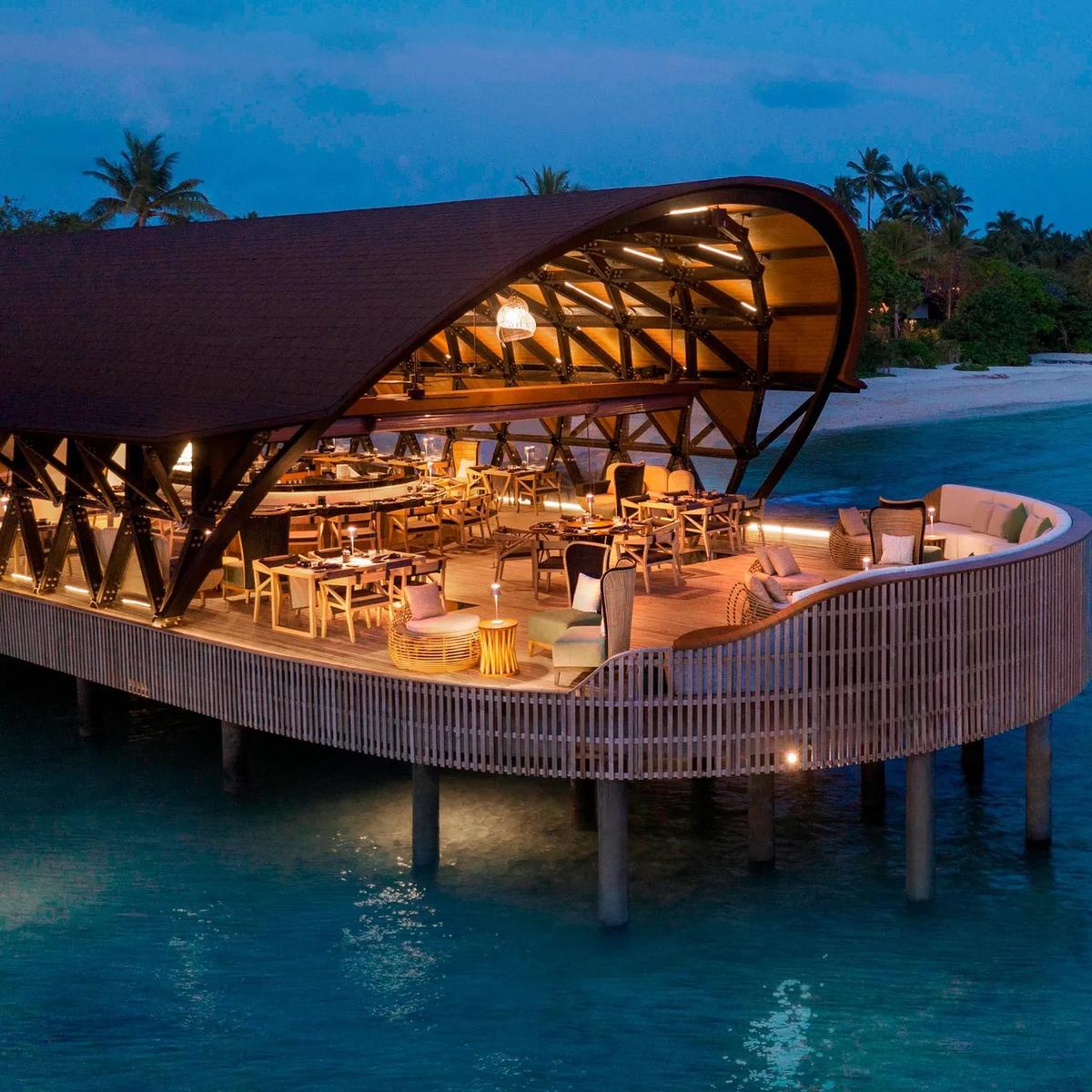 The resort's overwater dining pavilion at dusk, beach and jetty beyond