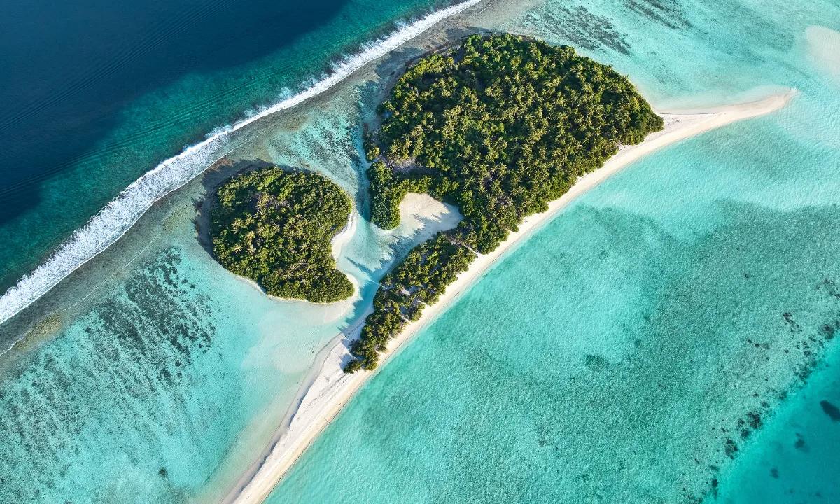 A small uninhabited sandbank island near Kandima, seen from above, fringed by reef and turquoise lagoon — the setting for the resort's Destination Dining castaway experience