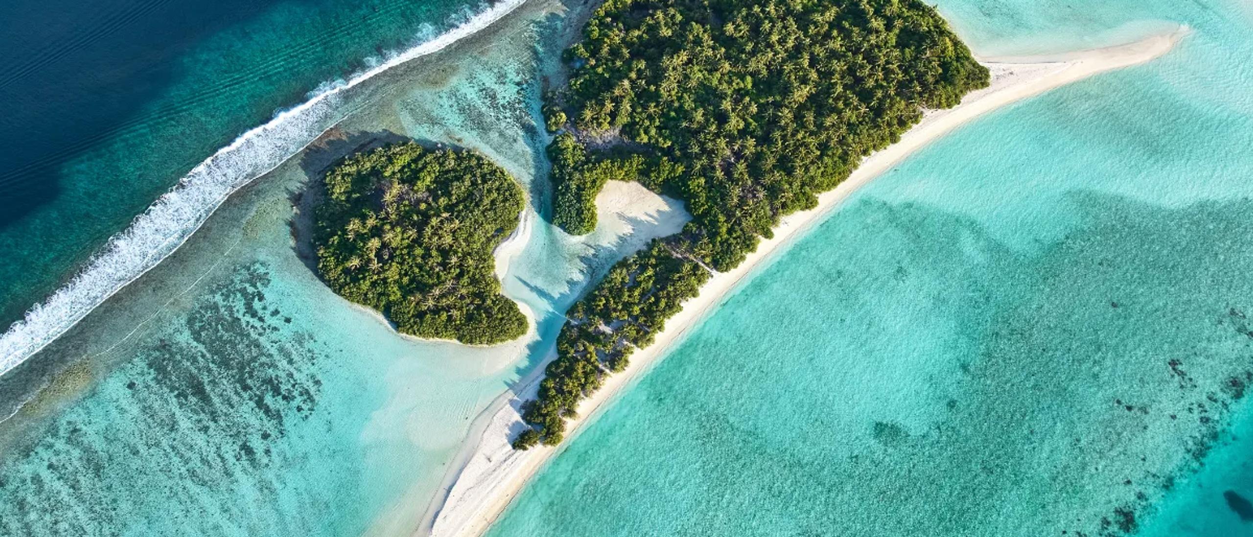 A small uninhabited sandbank island near Kandima, seen from above, fringed by reef and turquoise lagoon — the setting for the resort's Destination Dining castaway experience