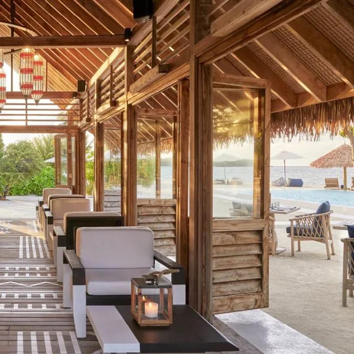 Faru Bar's counter, with a bartender at work and the pool and lagoon visible beyond